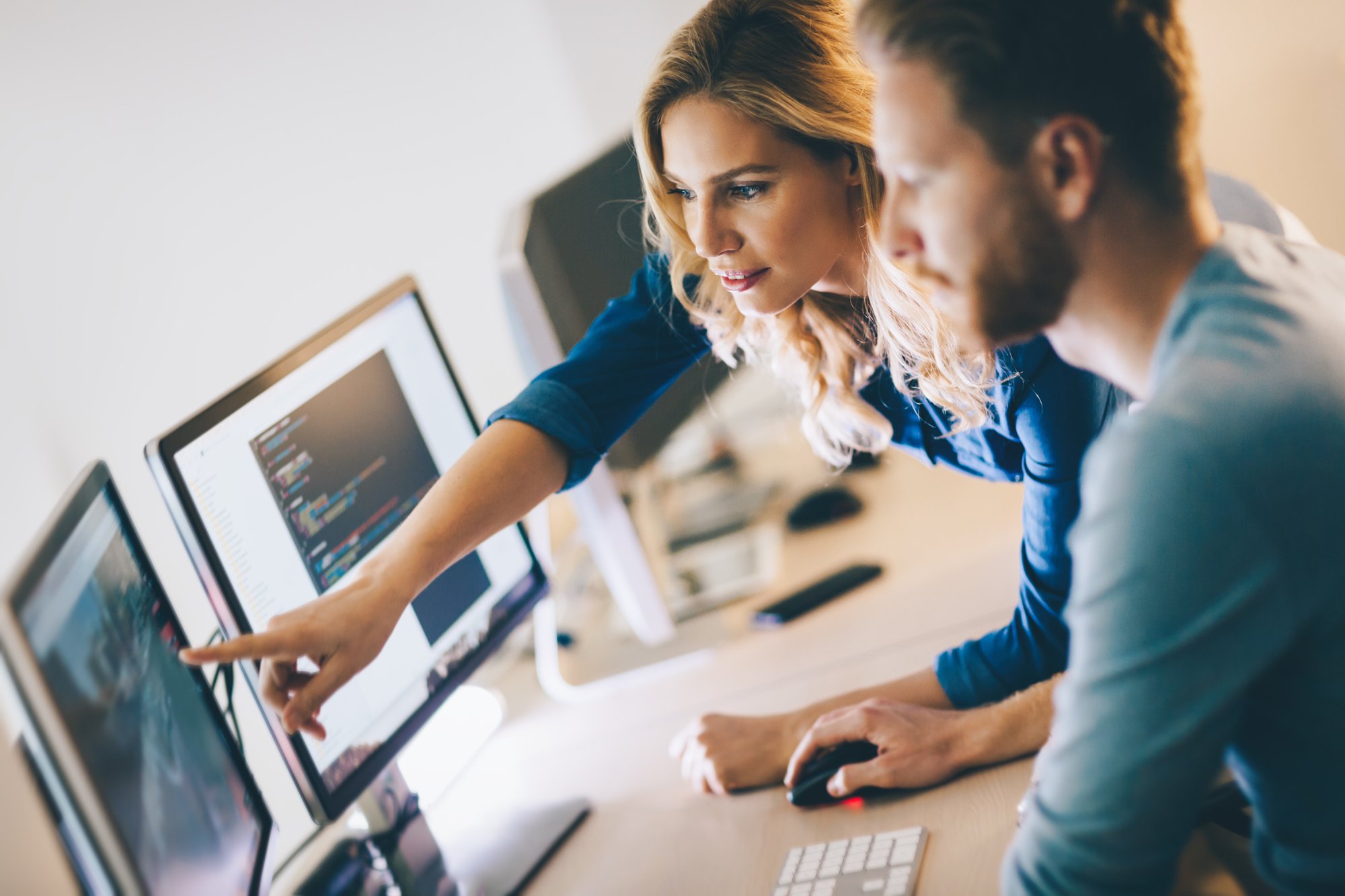 A woman is showing something to a man on a computer monitor