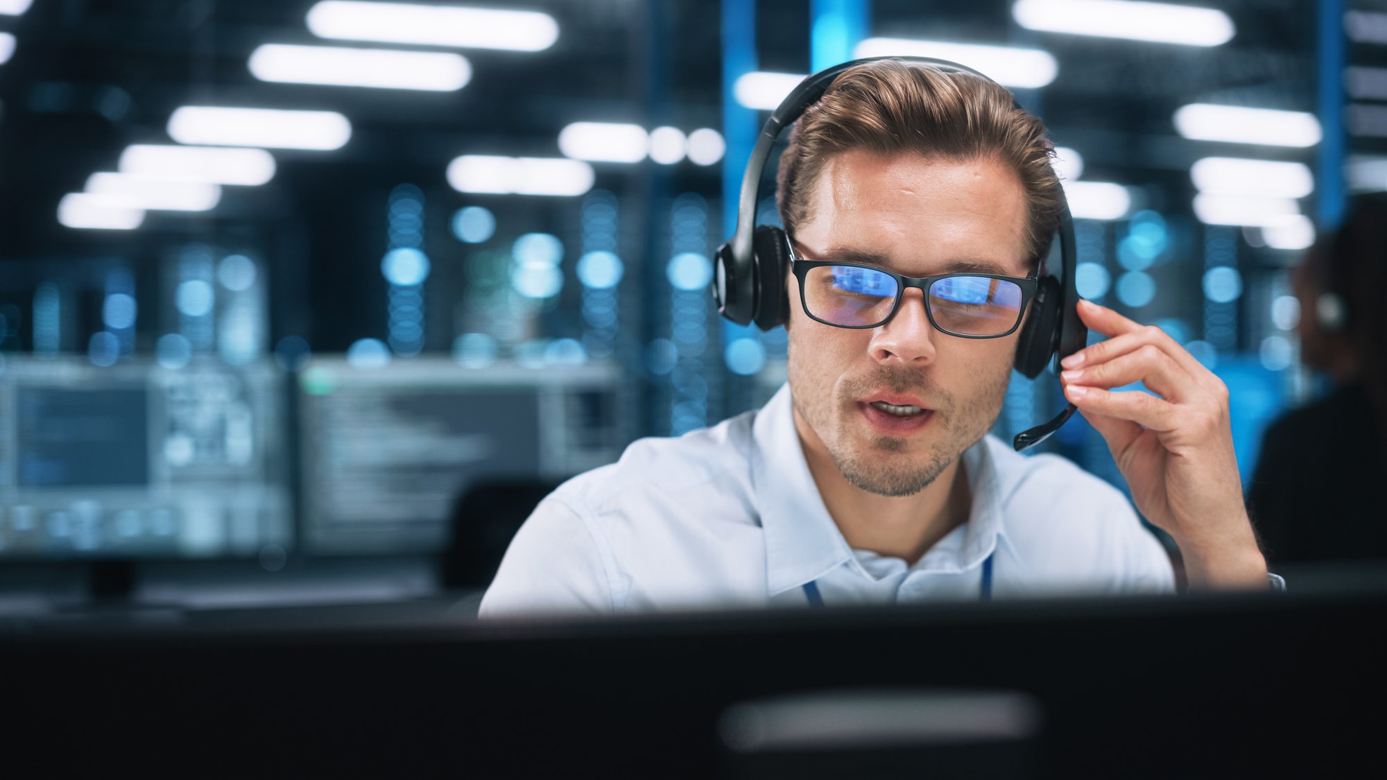 Mann sitzt mit Headset am Computer und spricht