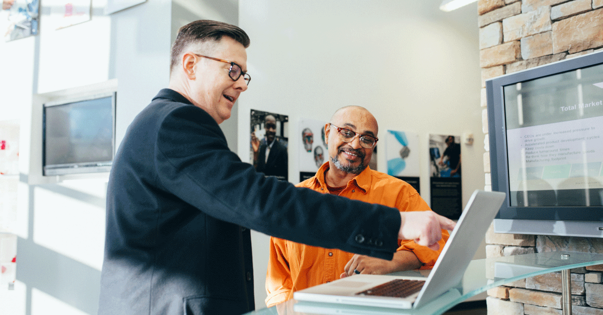 A man showing something to another man on a laptop