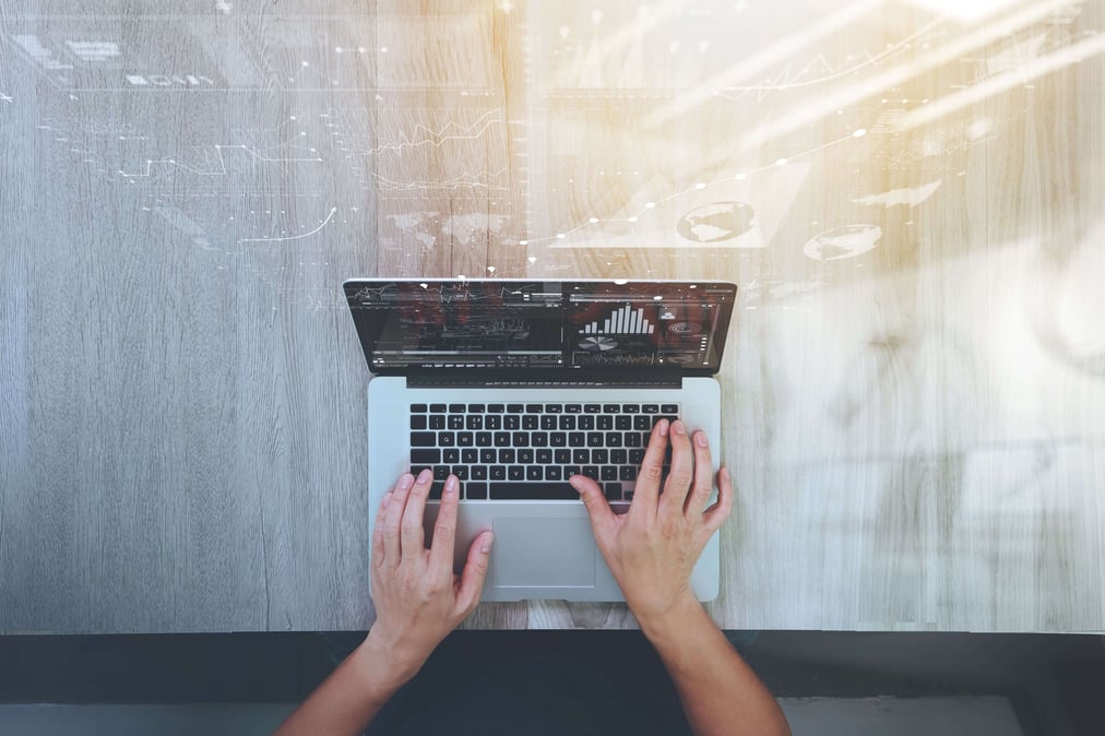 Photo of a laptop on a table with two human hands on it working, shot from bird perspective